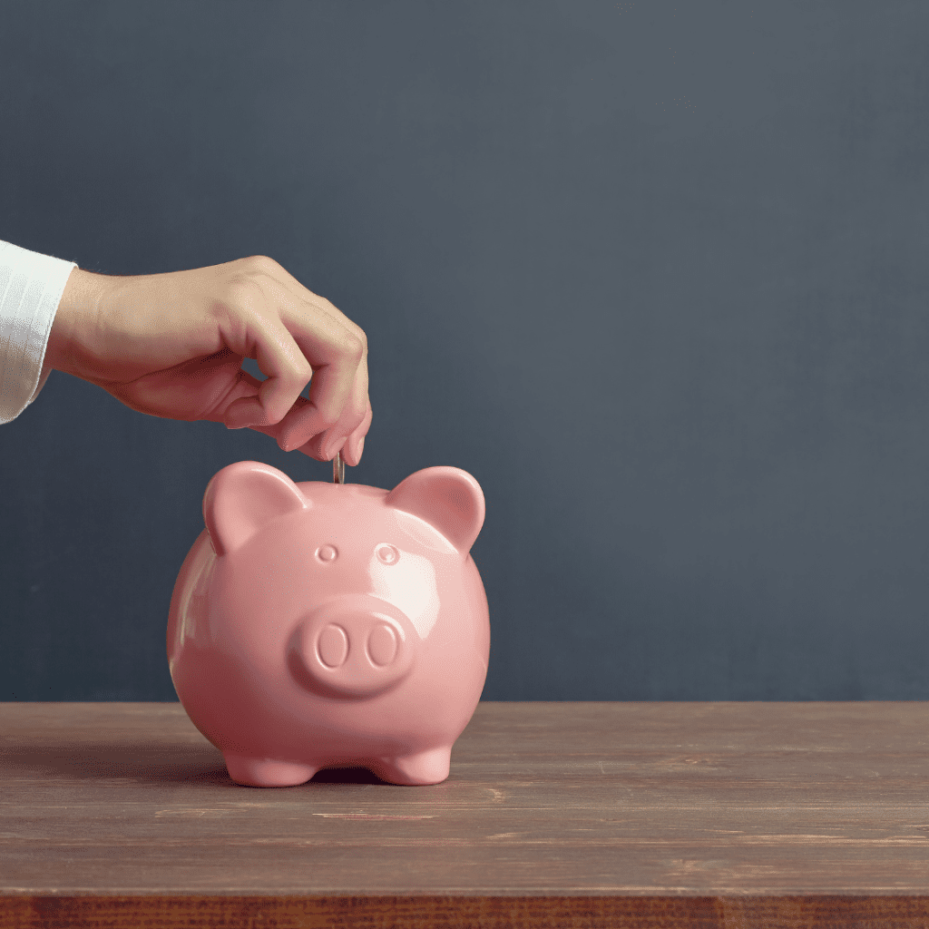 Hand placing a coin in a pink piggy bank.
